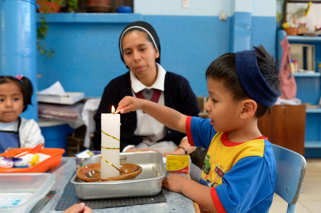 Schwester Guadalupe unterstützt Paulo, 3 Jahre, beim Anzünden einer Kerze, Montessori-Kindergarten und -Grundschule "Kinderhaus Santa Maria Magdalena Postel", Cochabamba, Departamento Cochabamba, Bolivien; Foto: Florian Kopp/SMMP